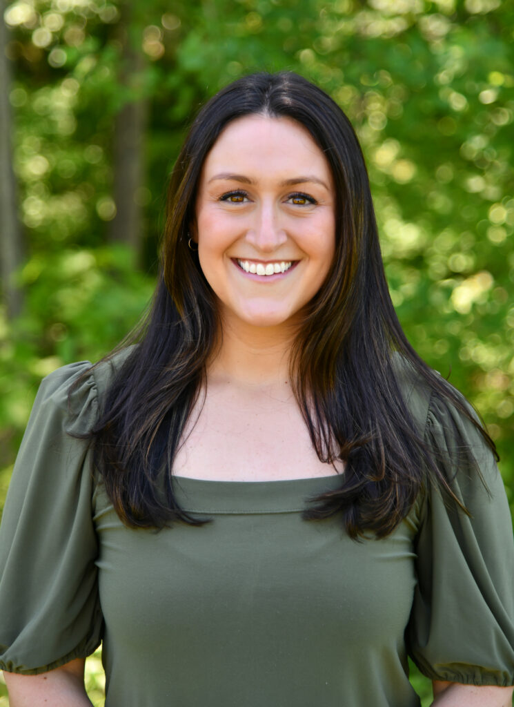 Smiling woman with long dark hair wearing a green blouse outdoors