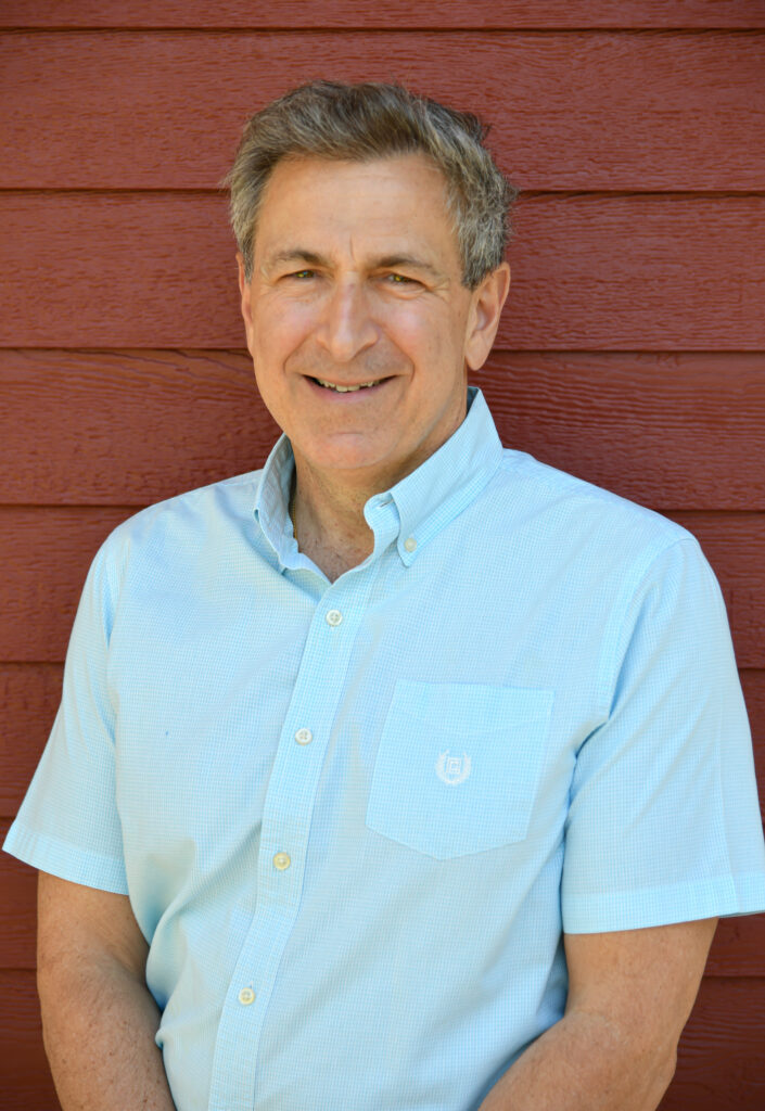 Smiling man in a light blue shirt standing in front of a red wooden wall